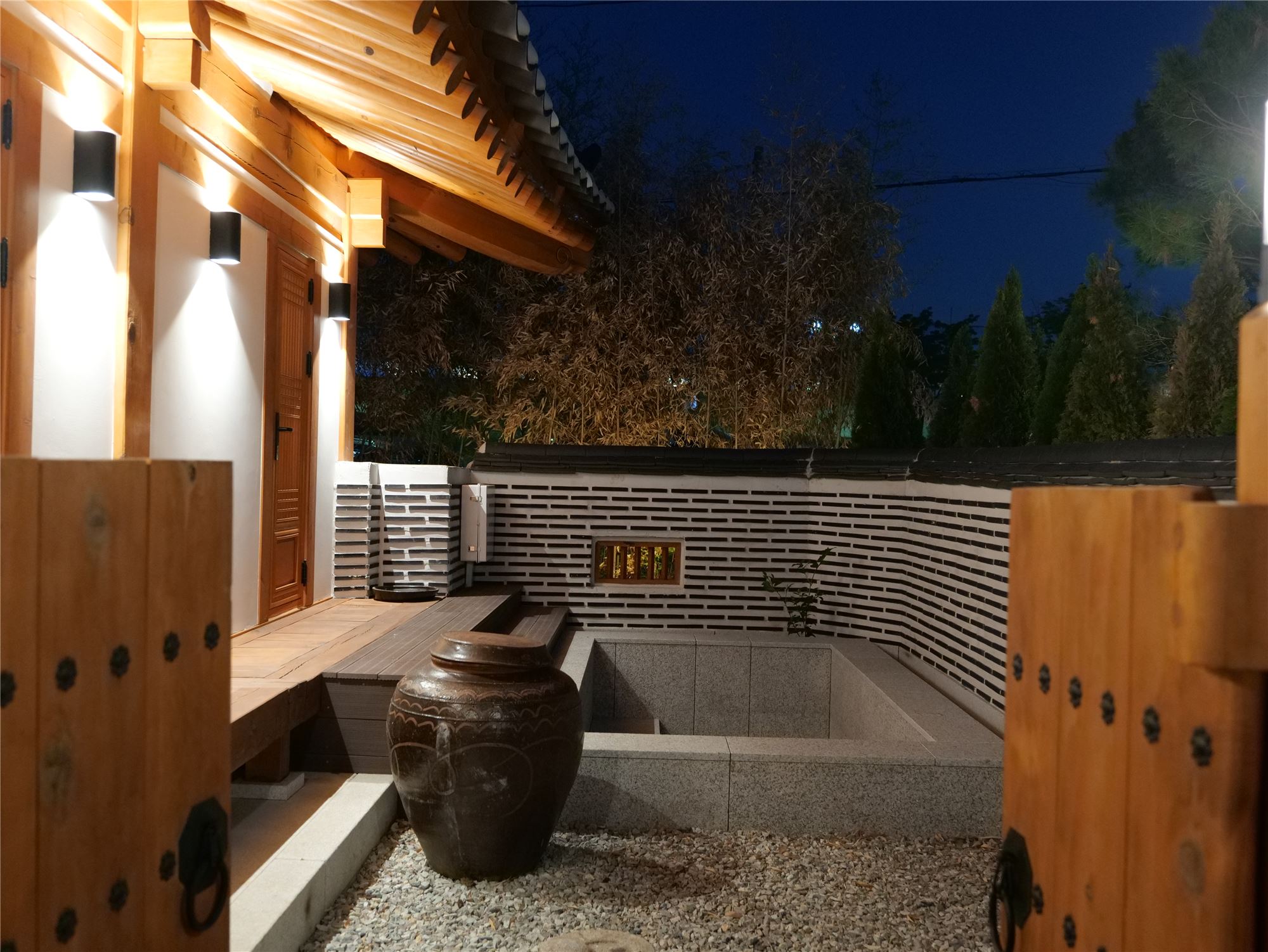 The private outdoor hot bath at night — bamboo and lanterns beyond the wall